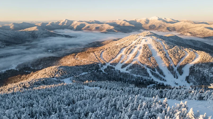 Artist's impression: an aerial view of an Adirondack ski mountain at golden hour, trails cut through forest